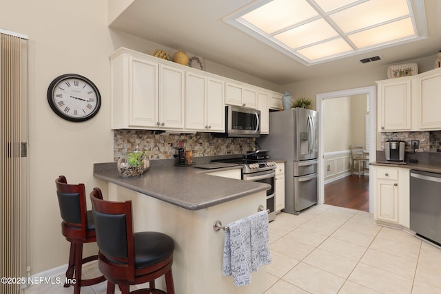 1766 Buttonbush Way, Fleming Island, FL 32003 - kitchen featuring appliances with stainless steel finishes, dark countertops, decorative backsplash, light tile patterned flooring, and a kitchen bar