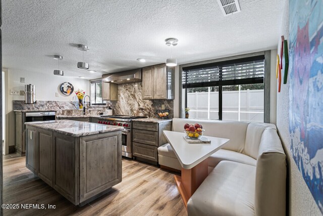 4 Santa Maria Ln, Saint Augustine, FL 32080 - kitchen with high end stove, a center island, wall chimney range hood, backsplash, and light wood-style floors