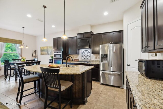 46 Gabacho Ct, Saint Augustine, FL 32095 - kitchen featuring stainless steel appliances, premium range hood, a breakfast bar area, light stone countertops, and dark brown cabinets
