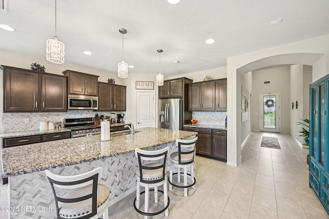 600 Broomsedge Cir, Saint Augustine, FL 32095 - kitchen with appliances with stainless steel finishes, tasteful backsplash, arched walkways, dark brown cabinets, and light stone countertops