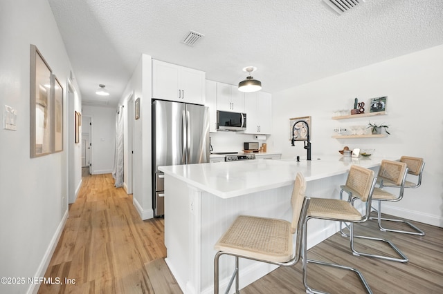 1848 Forsyth Ct, Atlantic Beach, FL 32233 - kitchen with appliances with stainless steel finishes, a breakfast bar, a peninsula, light wood finished floors, and white cabinetry