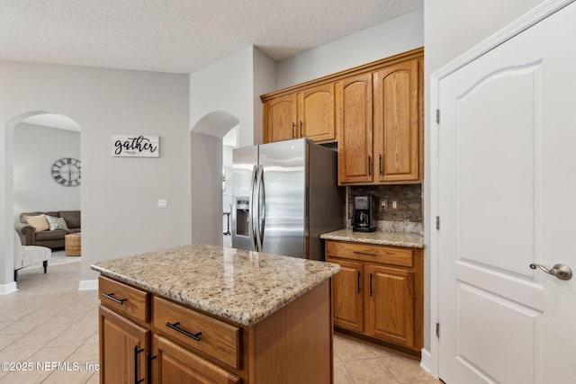 14220 Palmetto Springs St, Jacksonville, FL 32258 - kitchen with stainless steel fridge with ice dispenser, arched walkways, light tile patterned floors, decorative backsplash, and light stone countertops