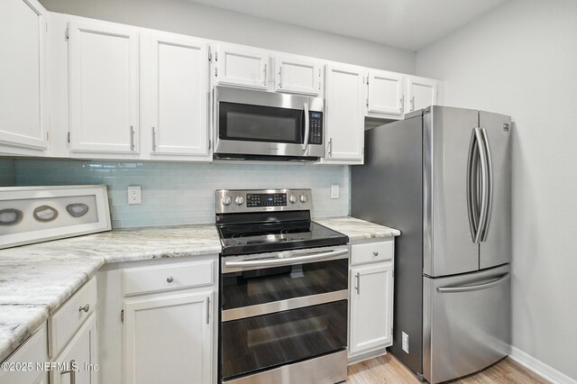 1800 The Greens Way Unit 603, Jacksonville Beach, FL 32250 - kitchen featuring appliances with stainless steel finishes, backsplash, white cabinetry, light wood-type flooring, and light stone counters