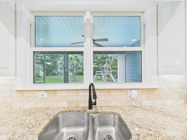 96168 High Pointe Dr, Fernandina Beach, FL 32034 - kitchen view of backsplash, light stone counters, white cabinetry, and a ceiling fan