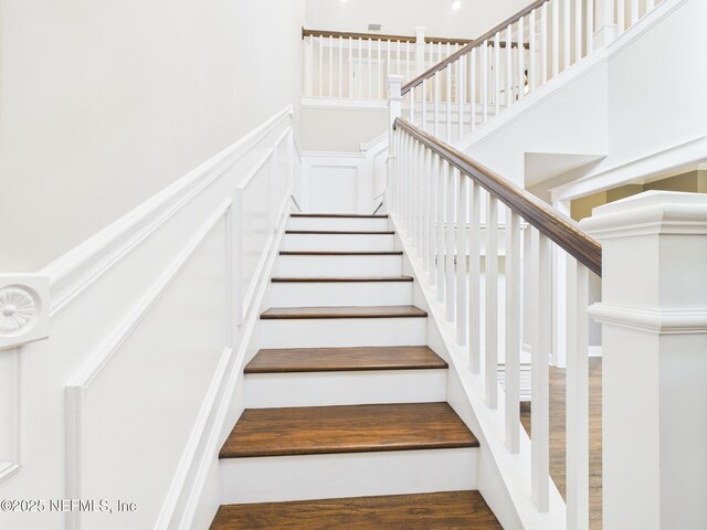 96168 High Pointe Dr, Fernandina Beach, FL 32034 - staircase with a decorative wall, a towering ceiling, wood finished floors, and wainscoting