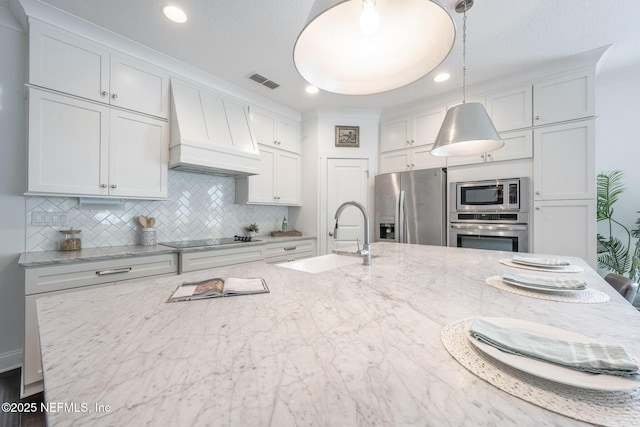 97082 Harbor Concourse Cir, Fernandina Beach, FL 32034 - kitchen with appliances with stainless steel finishes, premium range hood, tasteful backsplash, decorative light fixtures, and white cabinetry