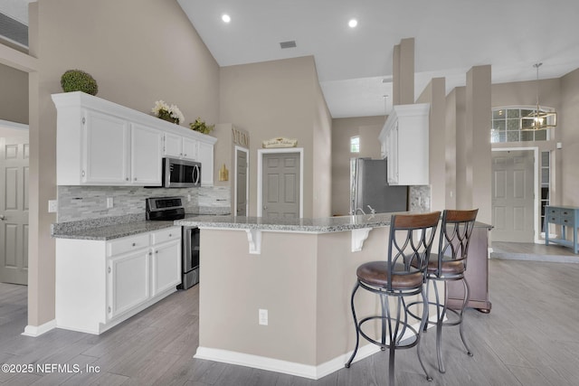 1571 Shelter Cove Dr, Fleming Island, FL 32003 - kitchen with appliances with stainless steel finishes, high vaulted ceiling, a peninsula, light wood finished floors, and backsplash