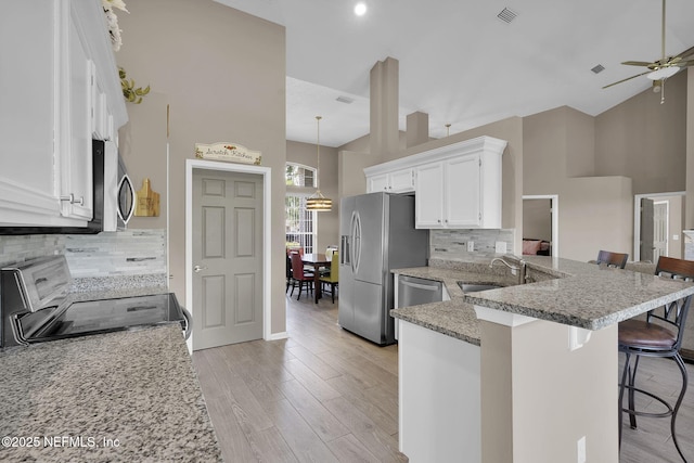 1571 Shelter Cove Dr, Fleming Island, FL 32003 - kitchen featuring appliances with stainless steel finishes, high vaulted ceiling, a kitchen bar, a peninsula, and white cabinets