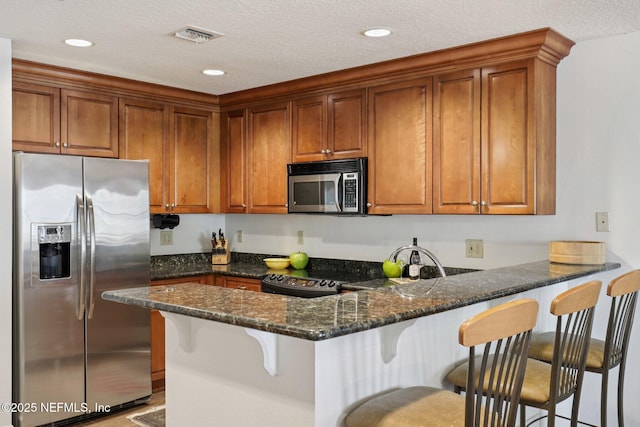 1478 Riverplace Blvd Unit 1605, Jacksonville, FL 32207 - kitchen featuring appliances with stainless steel finishes, a peninsula, brown cabinetry, dark stone counters, and recessed lighting