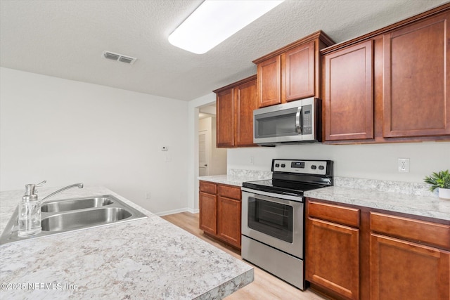 189 Blue Creek Way, Saint Augustine, FL 32086 - kitchen featuring appliances with stainless steel finishes, light wood-type flooring, light countertops, a textured ceiling, and brown cabinetry