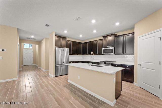 75570 Pondside Ln, Yulee, FL 32097 - kitchen featuring appliances with stainless steel finishes, light wood-style flooring, light countertops, a center island with sink, and decorative backsplash