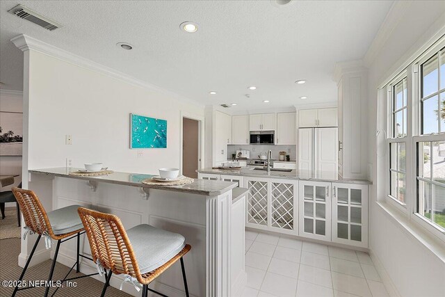 91 San Juan Dr Unit E3, Ponte Vedra Beach, FL 32082 - kitchen with appliances with stainless steel finishes, a peninsula, ornamental molding, white cabinets, and a kitchen breakfast bar