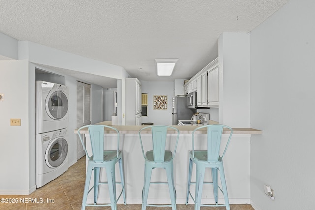 110 Ocean Hollow Ln Unit 114, Saint Augustine, FL 32084 - kitchen featuring stacked washer and clothes dryer, a peninsula, white cabinets, a kitchen breakfast bar, and a textured ceiling
