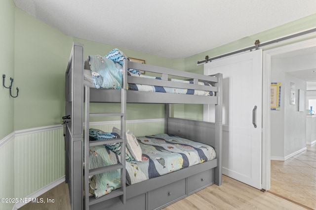 110 Ocean Hollow Ln Unit 114, Saint Augustine, FL 32084 - bedroom featuring a barn door, wainscoting, a textured ceiling, and wood finished floors