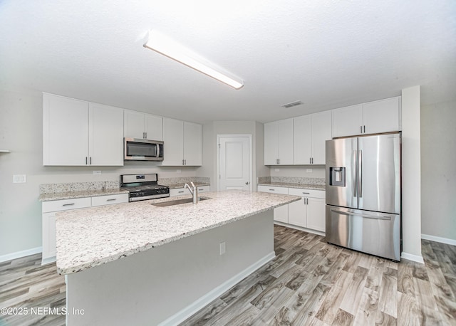 154 Moorcroft Way, Saint Augustine, FL 32092 - kitchen featuring appliances with stainless steel finishes, light wood-style floors, white cabinetry, an island with sink, and light stone countertops