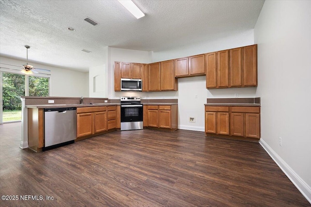 409 Spring Ridge Ct, Saint Augustine, FL 32092 - kitchen featuring appliances with stainless steel finishes, brown cabinetry, dark wood-style flooring, a peninsula, and a textured ceiling