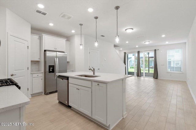 39 Thurnham Ln, Saint Augustine, FL 32092 - kitchen featuring appliances with stainless steel finishes, light wood finished floors, white cabinets, pendant lighting, and a kitchen island with sink
