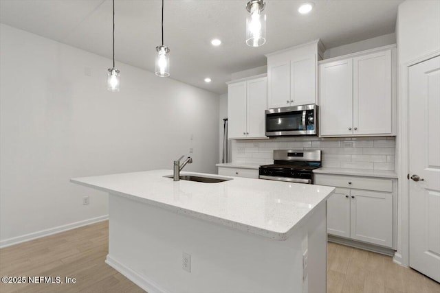 39 Thurnham Ln, Saint Augustine, FL 32092 - kitchen featuring appliances with stainless steel finishes, light wood-type flooring, decorative backsplash, white cabinets, and a kitchen island with sink