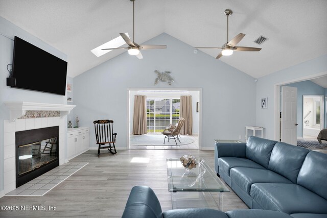 107 Hammock Cir, Saint Augustine, FL 32084 - living room with a ceiling fan, light wood-style flooring, a skylight, a tiled fireplace, and high vaulted ceiling