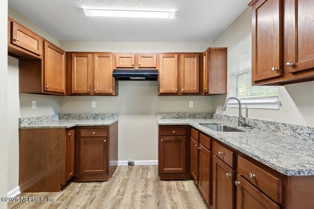 5522 Paris Ave, Jacksonville, FL 32209 - kitchen with under cabinet range hood, light wood finished floors, light stone counters, and brown cabinetry
