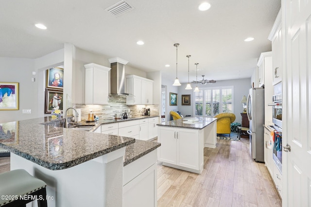 435 Tree Side Ln, Ponte Vedra, FL 32081 - kitchen featuring wall chimney exhaust hood, a peninsula, freestanding refrigerator, a center island, and light wood-type flooring
