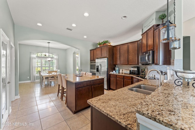 33114 Prairie Parke Pl, Fernandina Beach, FL 32034 - kitchen featuring appliances with stainless steel finishes, arched walkways, a kitchen island, light stone counters, and tasteful backsplash