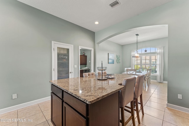 33114 Prairie Parke Pl, Fernandina Beach, FL 32034 - kitchen with a kitchen breakfast bar, arched walkways, light tile patterned flooring, light stone counters, and dark brown cabinets