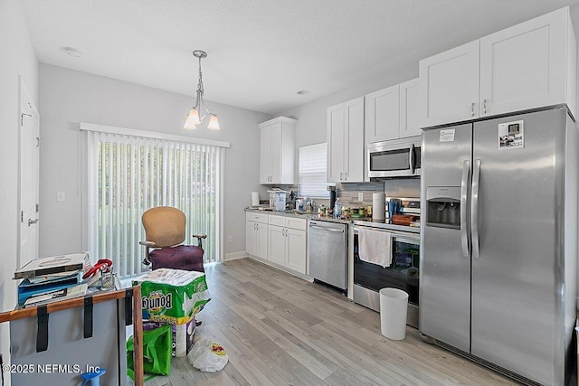 850 Bruen St, Saint Augustine, FL 32084 - kitchen with stainless steel appliances, light wood finished floors, white cabinetry, and hanging light fixtures