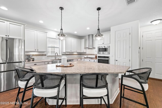 91 Paradise Valley Dr, Ponte Vedra, FL 32081 - kitchen with appliances with stainless steel finishes, wall chimney exhaust hood, a kitchen island, white cabinetry, and a breakfast bar area