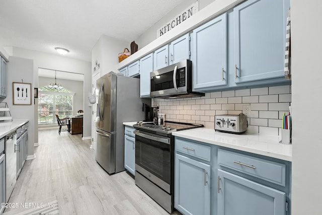 3172 Twilight Ct, Middleburg, FL 32068 - kitchen featuring appliances with stainless steel finishes, tasteful backsplash, light wood-style floors, light countertops, and blue cabinetry