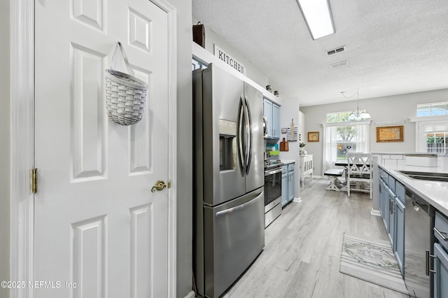 3172 Twilight Ct, Middleburg, FL 32068 - kitchen featuring stainless steel appliances, blue cabinets, light wood-style floors, light countertops, and a textured ceiling