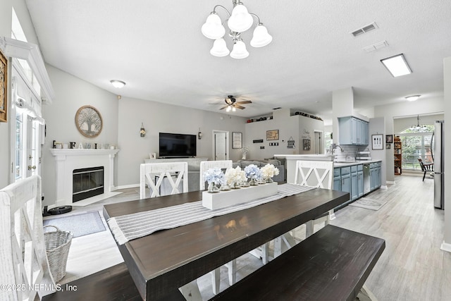 3172 Twilight Ct, Middleburg, FL 32068 - dining area featuring a chandelier, light wood-style flooring, a ceiling fan, and a fireplace with flush hearth