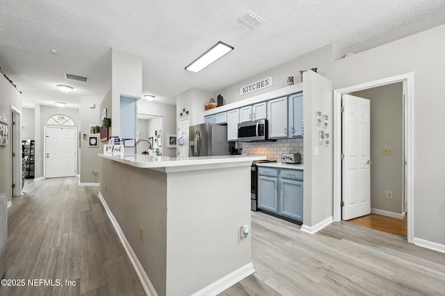 3172 Twilight Ct, Middleburg, FL 32068 - kitchen featuring stainless steel appliances, light wood-style flooring, blue cabinets, a peninsula, and a textured ceiling