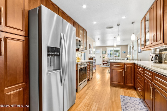 111 S 4th St, Fernandina Beach, FL 32034 - kitchen featuring appliances with stainless steel finishes, light wood-type flooring, glass insert cabinets, a peninsula, and brown cabinetry