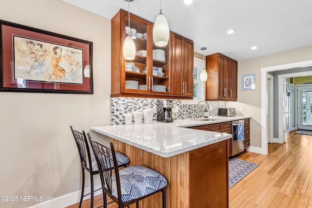 111 S 4th St, Fernandina Beach, FL 32034 - kitchen with brown cabinetry, tasteful backsplash, glass insert cabinets, light wood finished floors, and pendant lighting