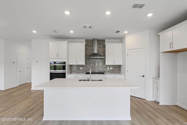 386 Whirlwind Pl, Saint Johns, FL 32095 - kitchen featuring wall chimney range hood, double oven, an island with sink, light countertops, and tasteful backsplash