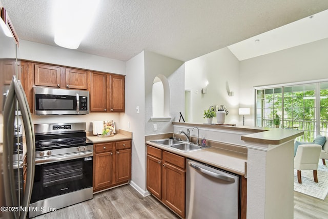 8550 Touchton Rd Unit 932, Jacksonville, FL 32216 - kitchen with appliances with stainless steel finishes, light wood-type flooring, a peninsula, brown cabinetry, and a textured ceiling