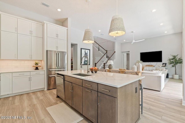 351 Palm Crst Dr, Ponte Vedra, FL 32081 - kitchen with appliances with stainless steel finishes, white cabinets, an island with sink, decorative backsplash, and light wood-type flooring