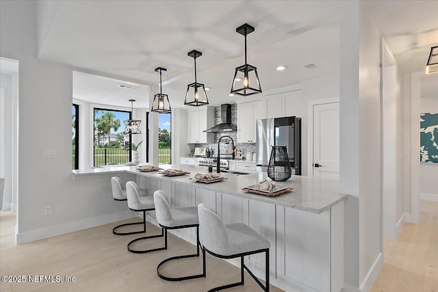172 Laurel Ln, Ponte Vedra Beach, FL 32082 - kitchen with freestanding refrigerator, wall chimney range hood, white cabinets, light wood finished floors, and backsplash