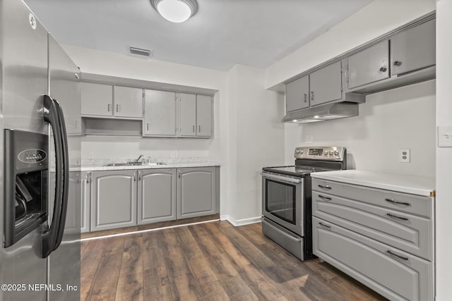 7314 Hielo Dr, Jacksonville, FL 32211 - kitchen with stainless steel appliances, gray cabinetry, under cabinet range hood, dark wood-style flooring, and light countertops
