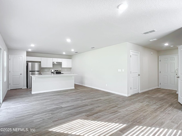 29 Wood Ash Ln, Palm Coast, FL 32164 - kitchen with freestanding refrigerator, light wood-style flooring, an island with sink, white cabinetry, and light countertops