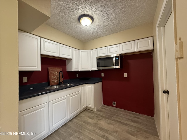 1406 W 18th St, Jacksonville, FL 32209 - kitchen featuring stainless steel microwave, a textured ceiling, dark countertops, light wood-style floors, and white cabinetry