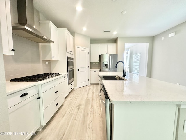 356 Bermudez Way, Saint Augustine, FL 32095 - kitchen with wall chimney range hood, appliances with stainless steel finishes, light wood-style flooring, a kitchen island with sink, and tasteful backsplash