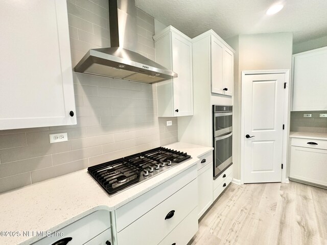 356 Bermudez Way, Saint Augustine, FL 32095 - kitchen featuring wall chimney exhaust hood, appliances with stainless steel finishes, white cabinetry, light wood finished floors, and tasteful backsplash