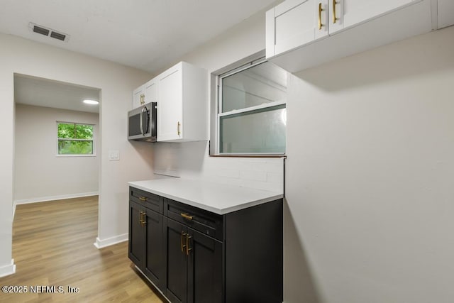 9340 Norfolk Blvd, Jacksonville, FL 32208 - kitchen featuring white cabinets, stainless steel microwave, light countertops, decorative backsplash, and light wood-style floors