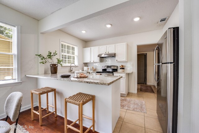 3516 Myra St, Jacksonville, FL 32205 - kitchen featuring stainless steel appliances, under cabinet range hood, white cabinets, backsplash, and a peninsula