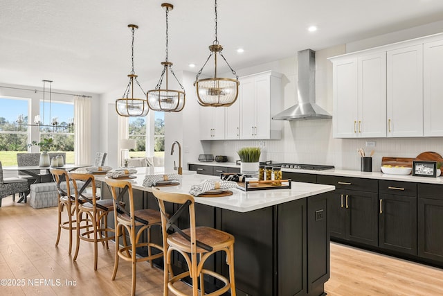 80 Oak Cluster Ln, Saint Augustine, FL 32092 - kitchen featuring wall chimney exhaust hood, light countertops, light wood-style flooring, white cabinets, and a kitchen breakfast bar