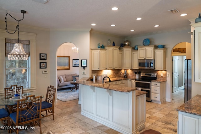 13464 Ellsworth Ln, Jacksonville, FL 32225 - kitchen with stainless steel appliances, arched walkways, cream cabinetry, a peninsula, and recessed lighting