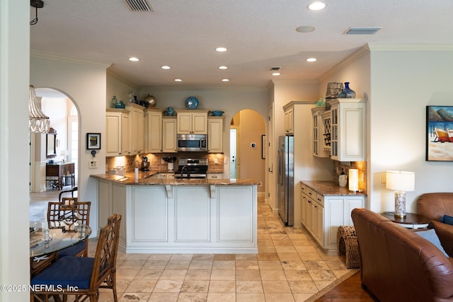 13464 Ellsworth Ln, Jacksonville, FL 32225 - kitchen featuring arched walkways, appliances with stainless steel finishes, cream cabinetry, backsplash, and a peninsula