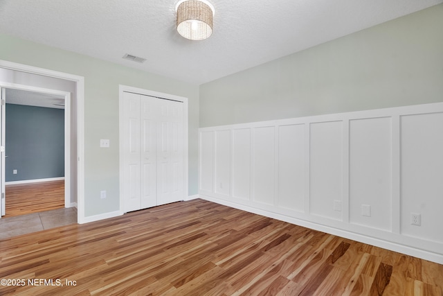 429 N Bridgestone Ave, Saint Johns, FL 32259 - unfurnished bedroom with light wood-style floors, a decorative wall, a wainscoted wall, a closet, and a textured ceiling